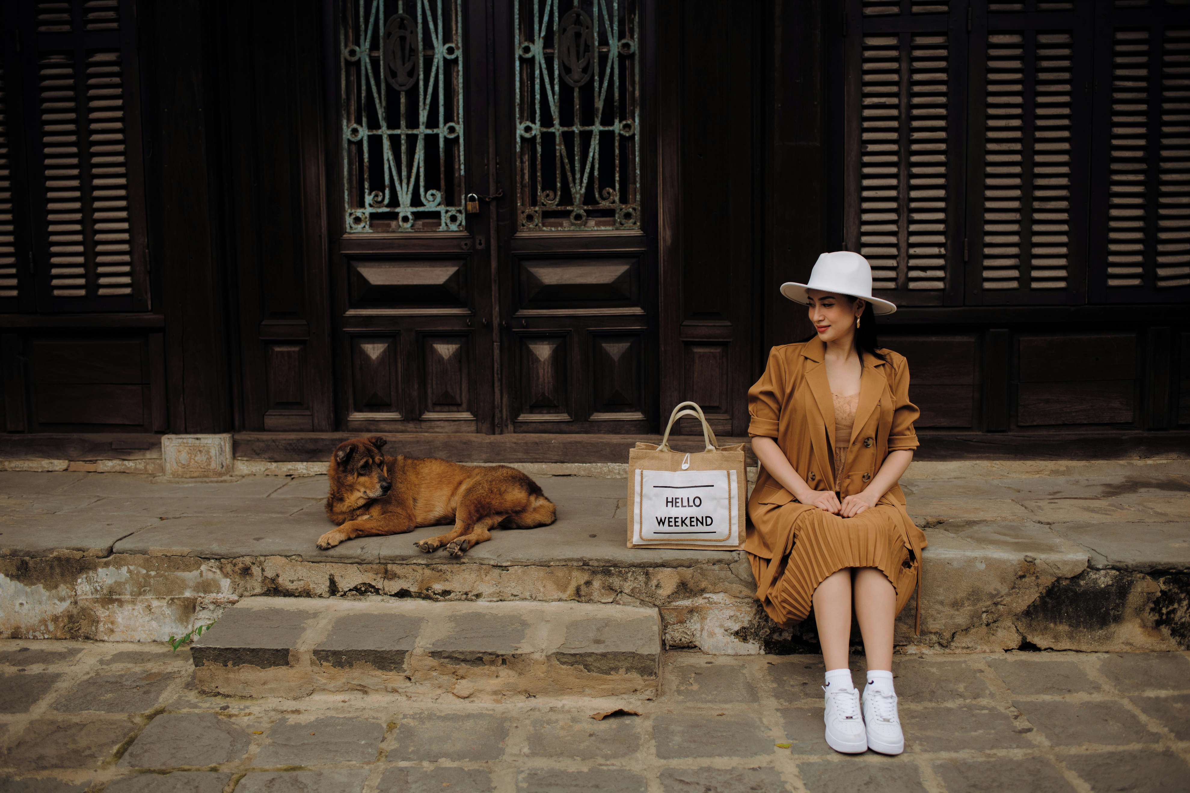 A digital nomad sits on the sidewalk beside her dog.